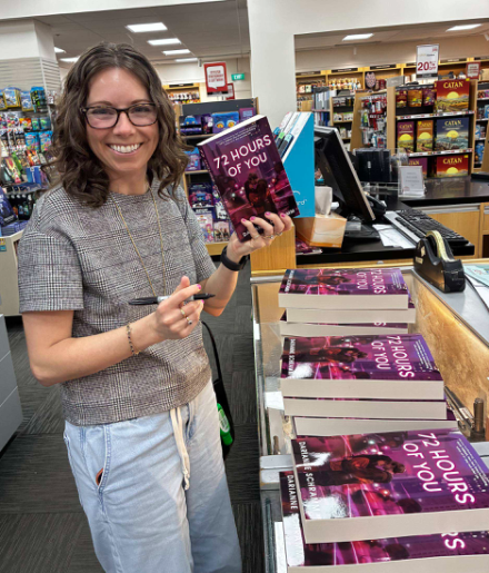 Darianne Schramm holding her debut and a sharpie as she signs copies of her debut novel.
